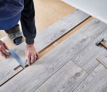 Man preparing laminate plank for floor installation in apartment under renovation. Close up of male construction worker using metal ruler and pencil while drawing line on laminate flooring board.